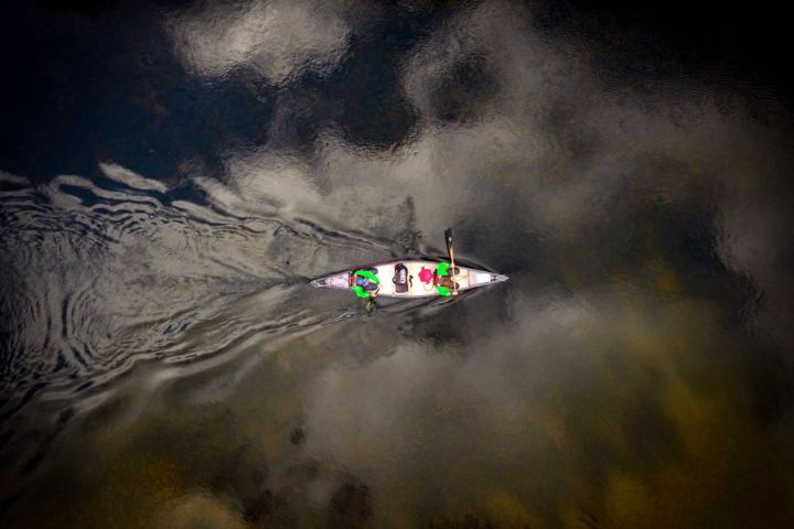 Aerial view of a canoe with two people paddling on a reflective water surface.