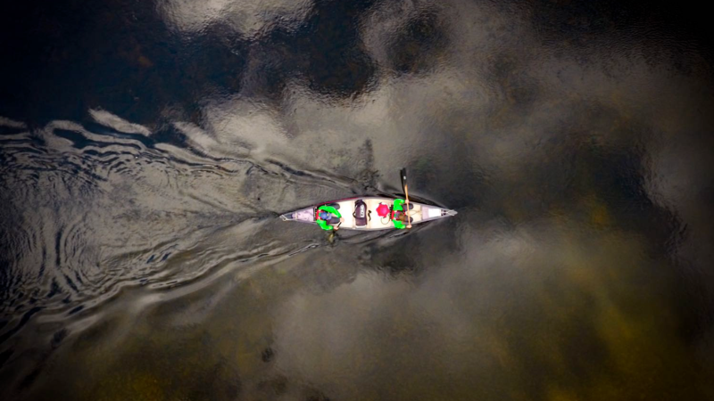 Aerial view of a canoe with two people paddling on a reflective water surface.