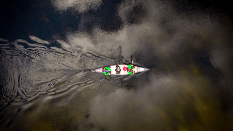 Aerial view of a canoe with two people paddling on a calm, reflective water surface.