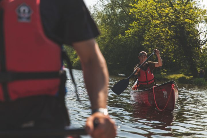 Two people paddling red canoes on a sunny day, one closer to the camera.