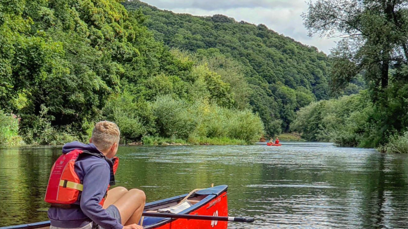 Person in red canoe paddling on a calm river surrounded by lush green trees.