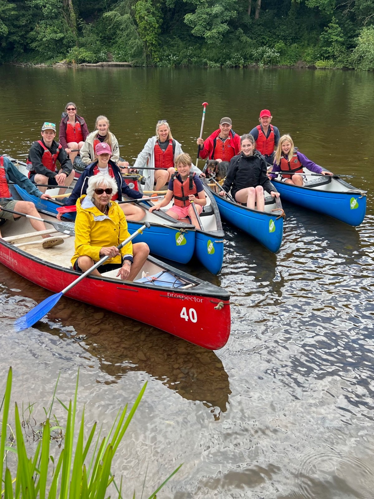 Group of people in canoes on a river near a forested bank.