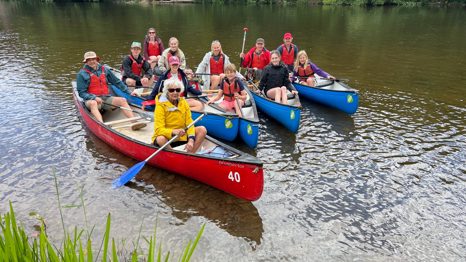 Group of people in canoes on a river near a forested bank.