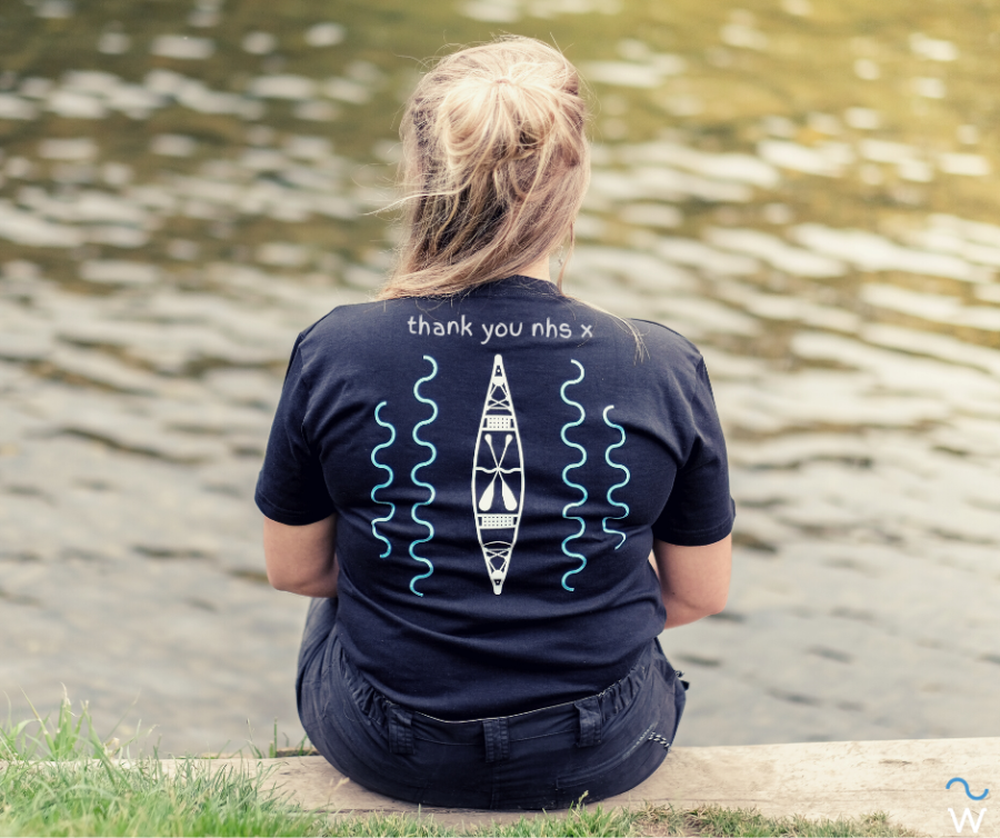 Person in blue shirt with 'thank you nhs' text sits by water edge.
