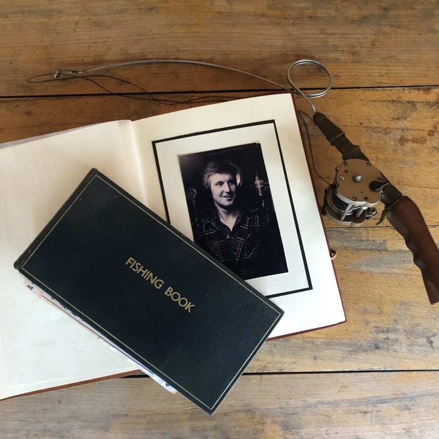 Open photo album with a portrait, fishing book, and rod on a wooden table.