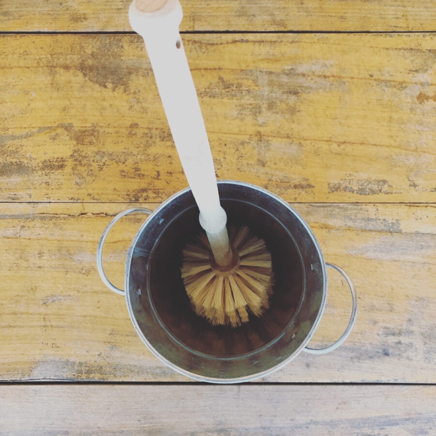 Top view of a brush in a metal bucket on a wooden surface.