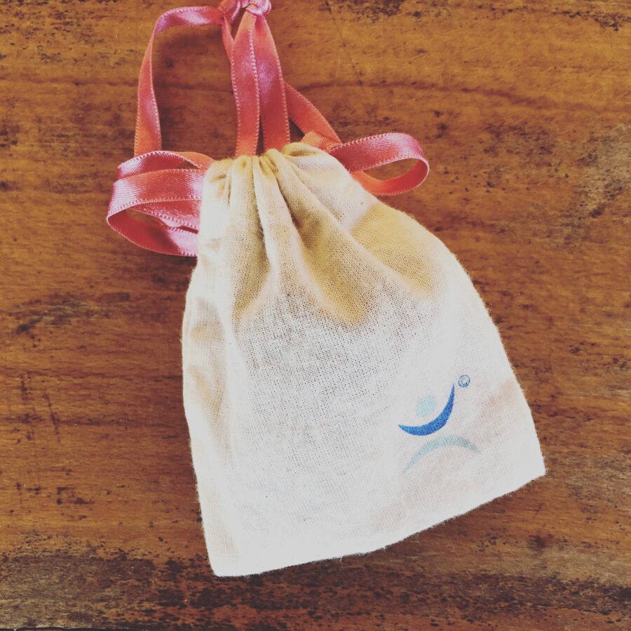 Small cloth bag with pink ribbons on a wooden surface.