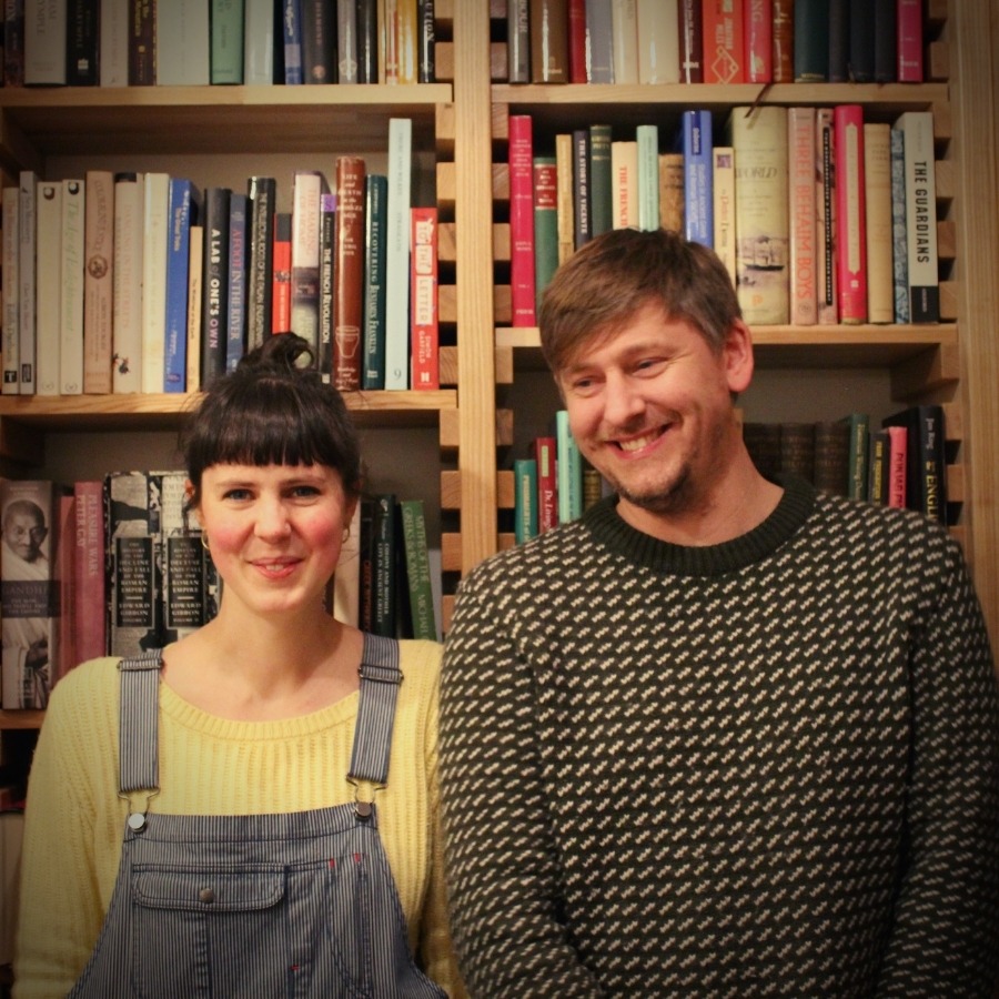 Two smiling people in front of a bookshelf filled with books.