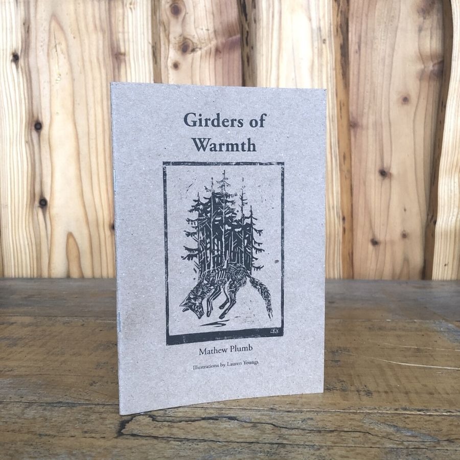 Book titled 'Girders of Warmth' on wooden surface, cover shows illustration of a forest and wolf.
