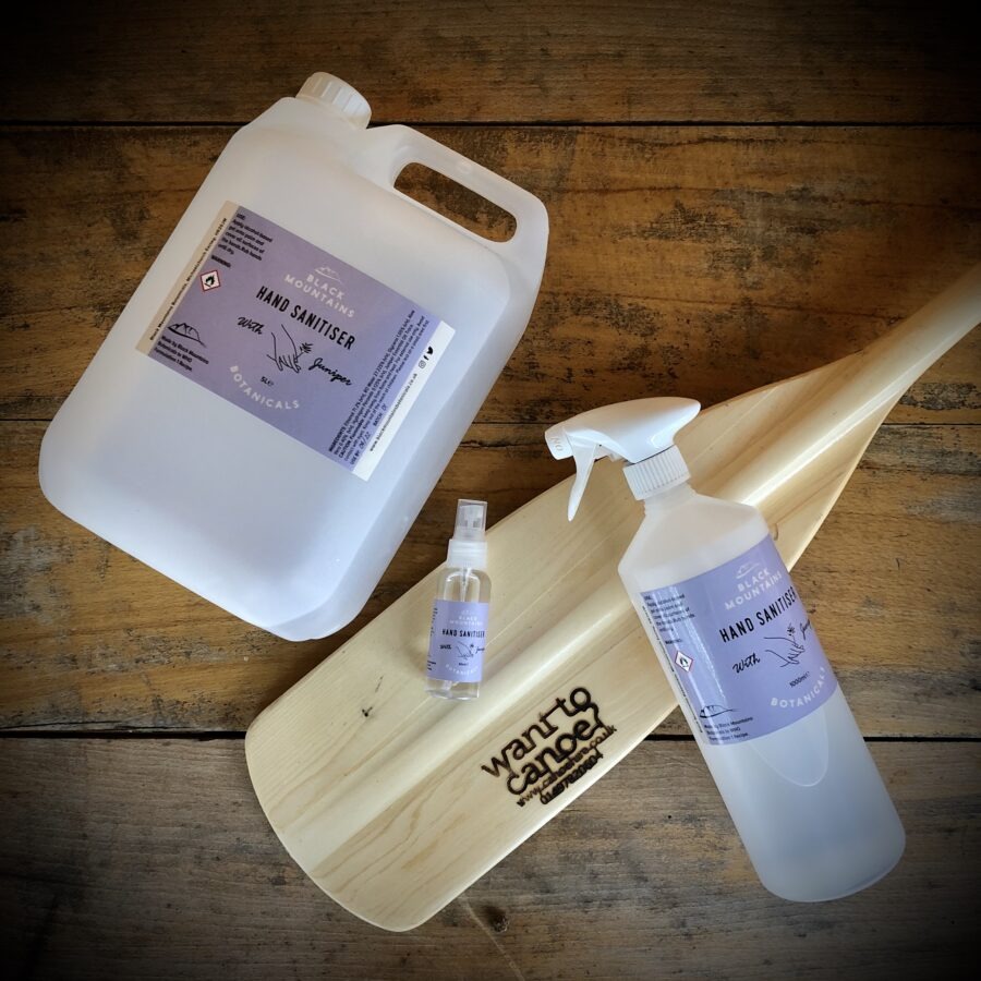 Three bottles of hand sanitizer on a wooden paddle with a 'Want to Canoe?' engraving.