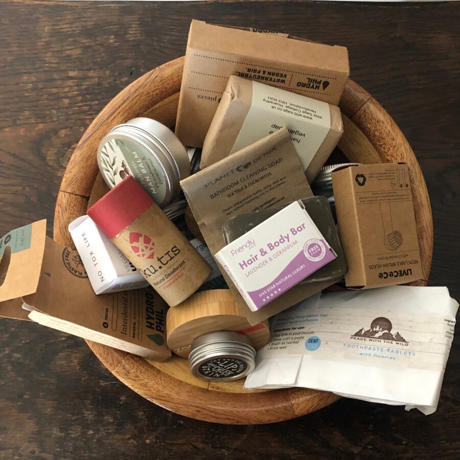 Wooden bowl with assorted eco-friendly toiletries and packaging on a wooden surface.