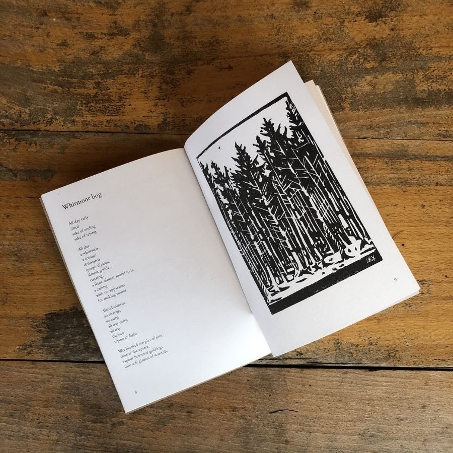 Open book on wooden surface with poem on left and forest illustration on right.