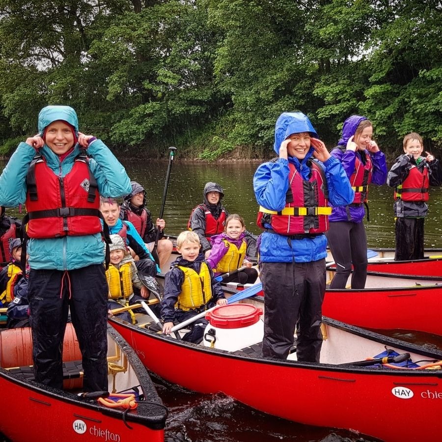 Group of people in rain gear smiling in canoes on a river.