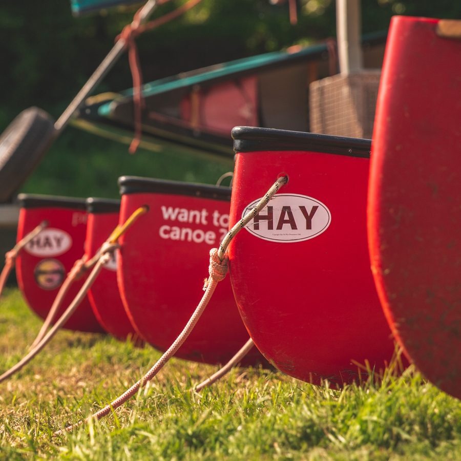 Red canoes lined up on grass, featuring 'HAY' stickers and ropes.