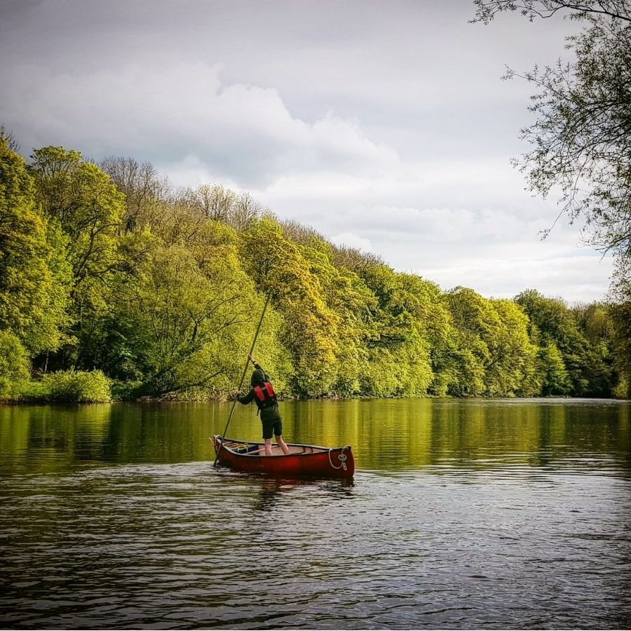 Person in red canoe paddling on a calm river with green trees lining the shore.