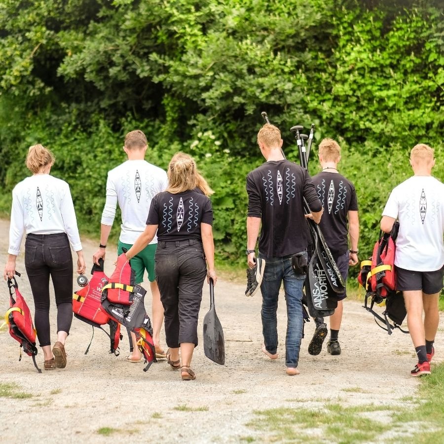 Six people walking away, carrying paddles and life jackets, wearing matching shirts.