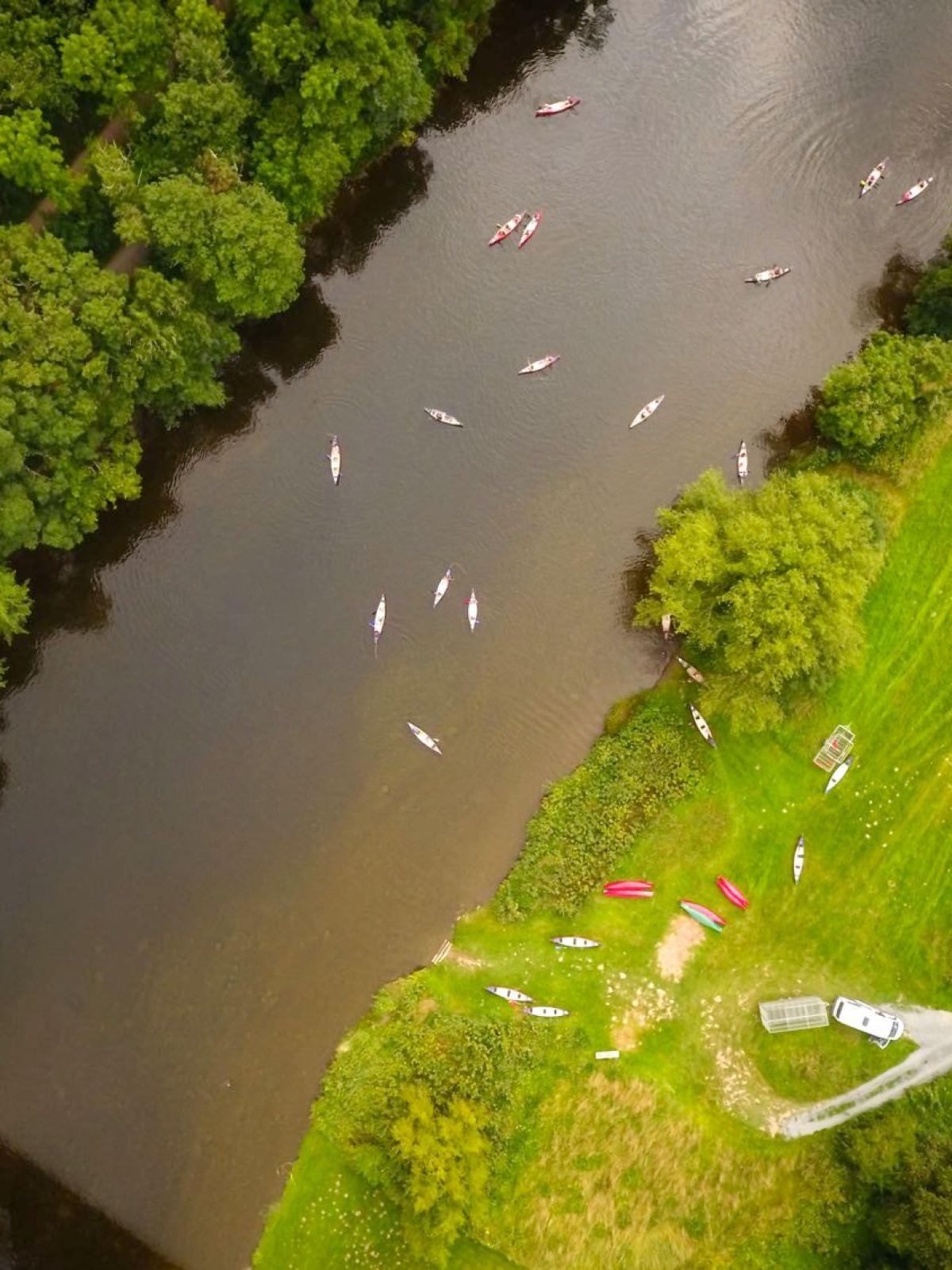 Aerial view of boats on a river surrounded by trees and grassy fields.
