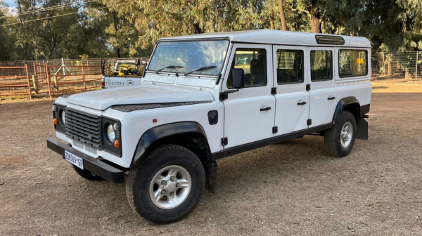 White SUV with off-road capabilities parked on dirt path with trees in background.
