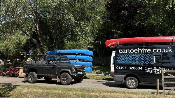 Pickup truck with blue canoes and a van in a grassy area with trees.